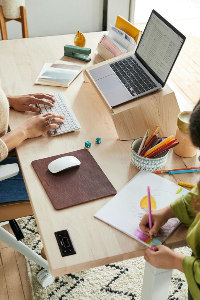 Two women sit around a table, strategizing over a laptop and notebooks.